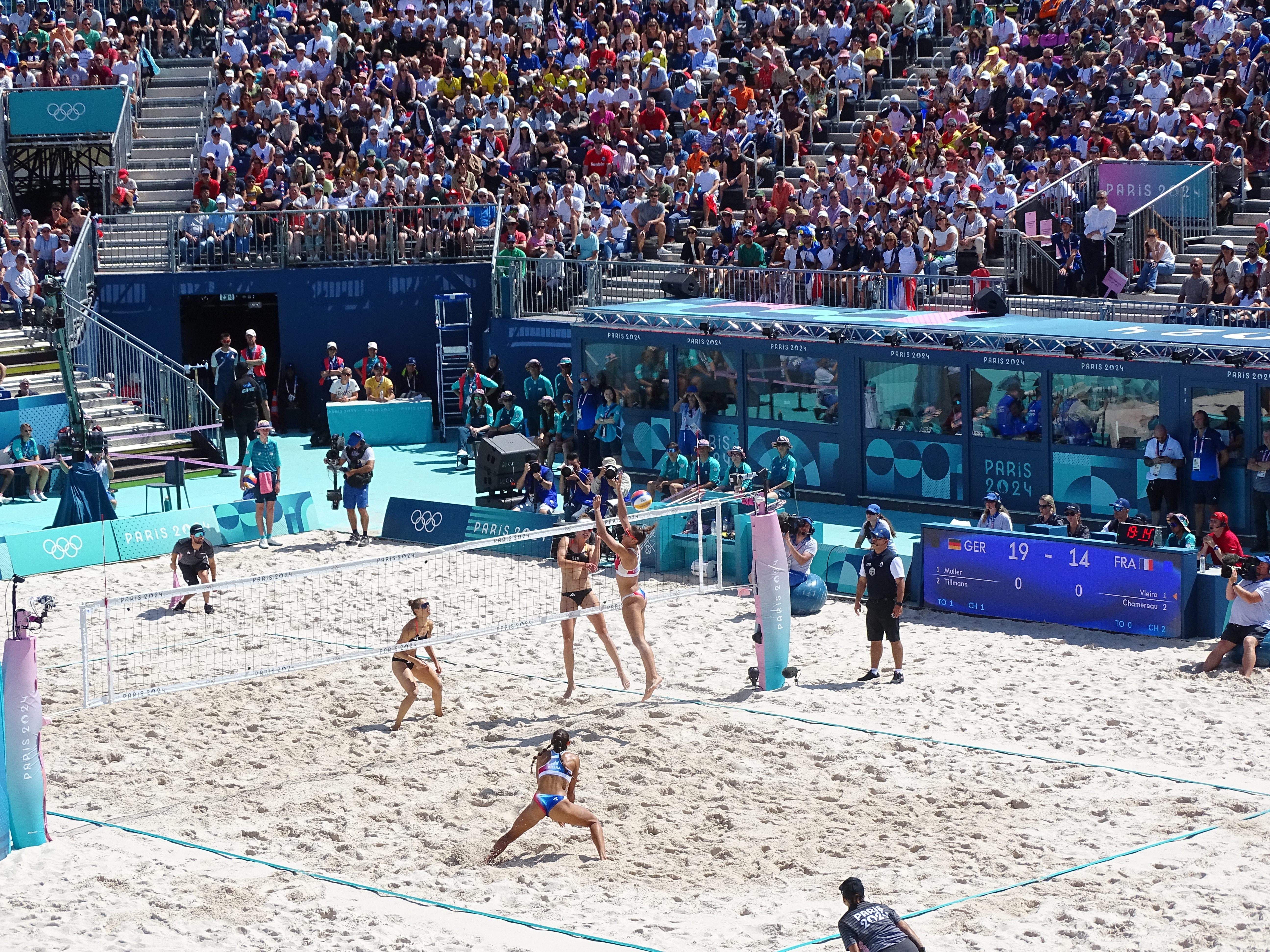 Jogadoras disputam a bola junto à rede em uma partida de vôlei de praia.