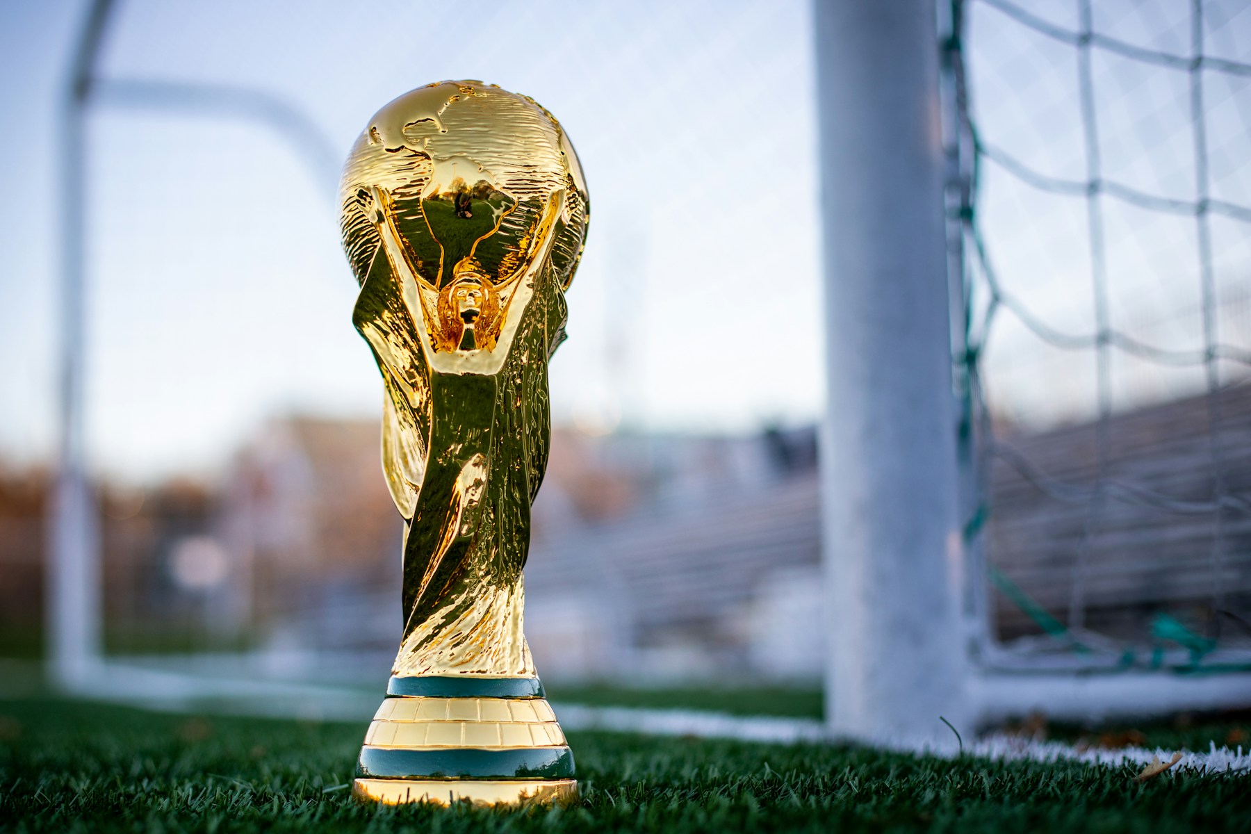 Réplica dourada da taça da Copa do Mundo sobre o gramado, próxima a uma trave.