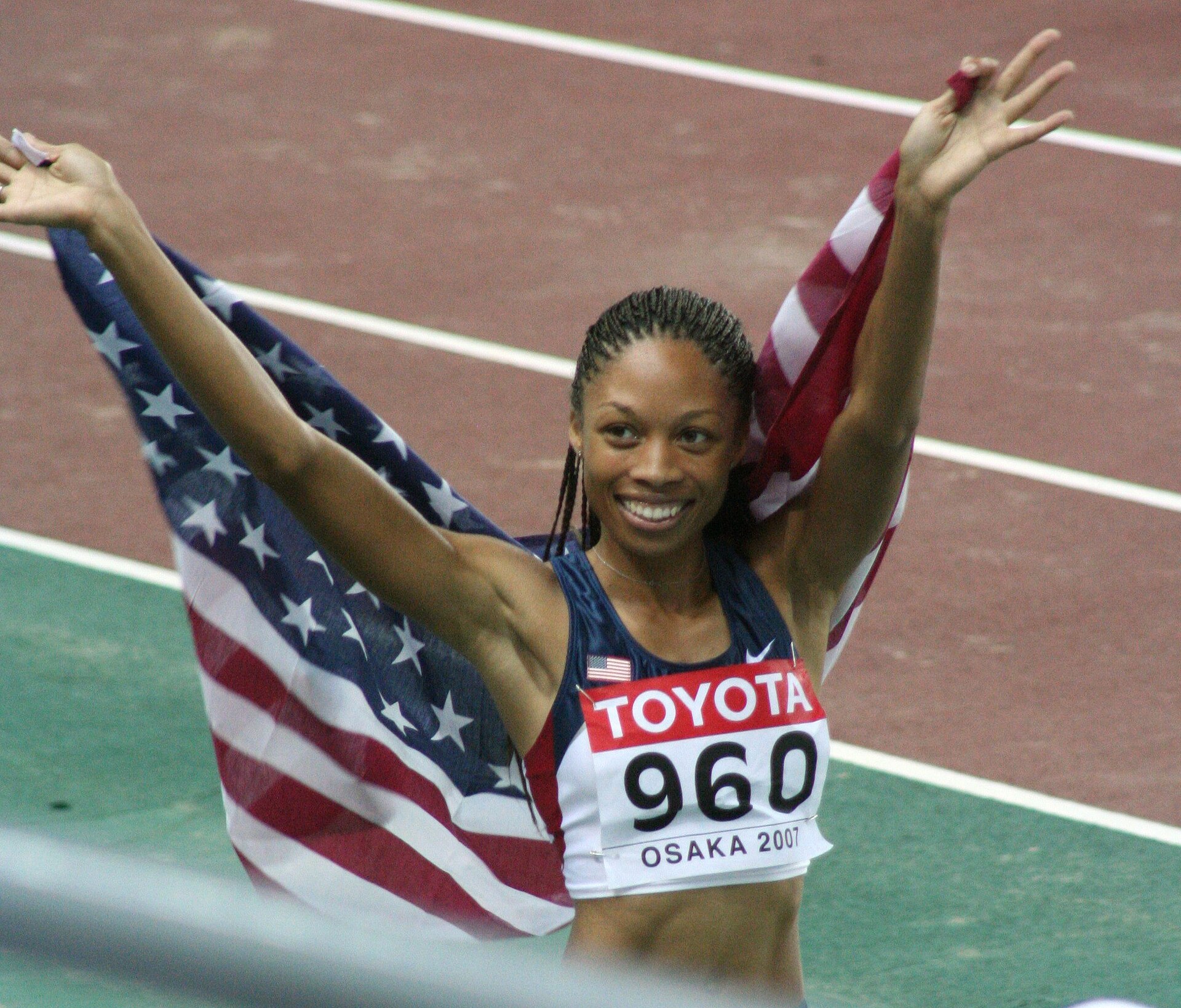 Allyson Felix sorri com os braços erguidos e a bandeira dos Estados Unidos após vencer os 200 metros femininos em Osaka 2007.