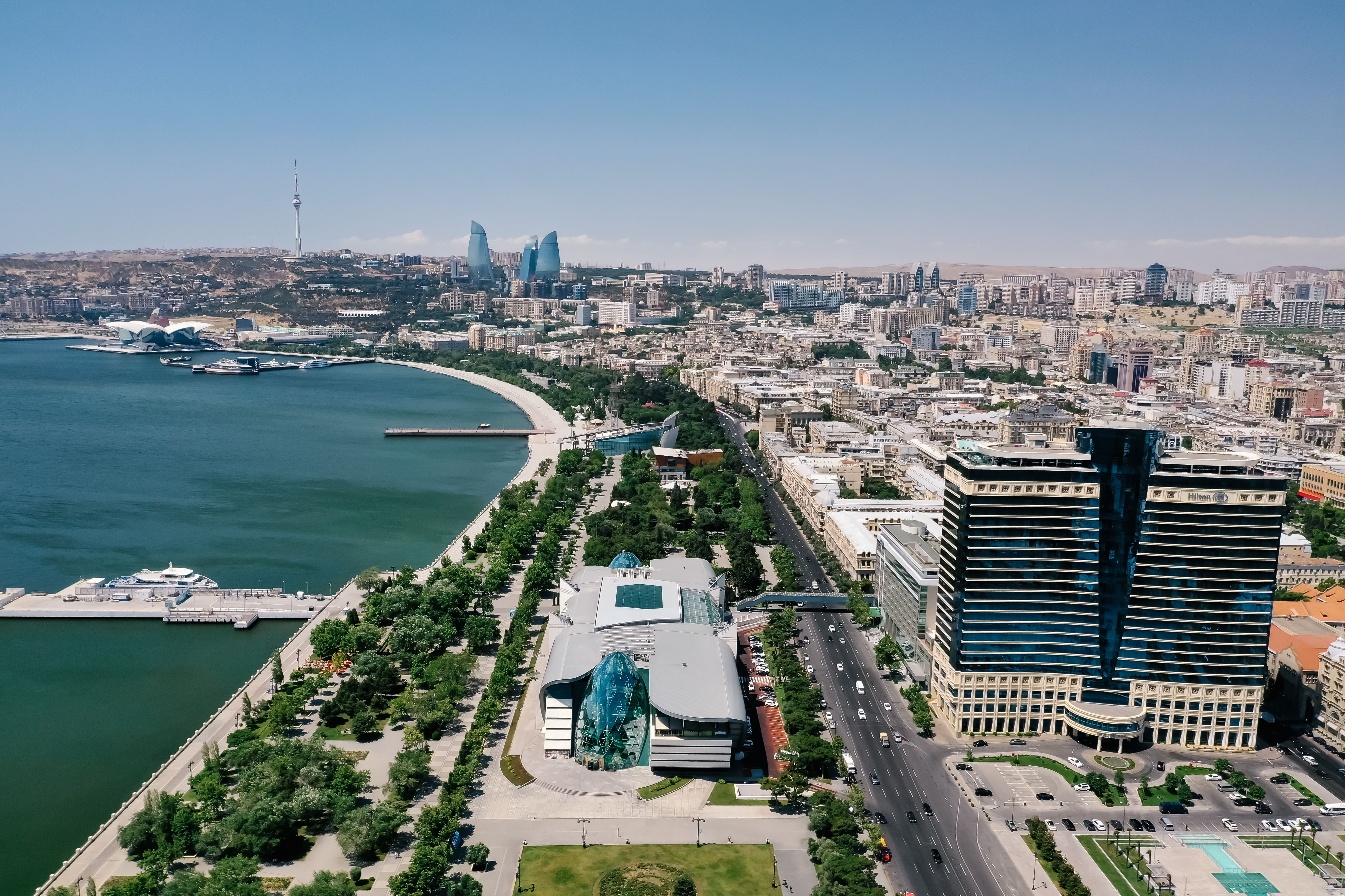 Vista aérea de Baku com o Mar Cáspio, avenida arborizada e edifícios da cidade.