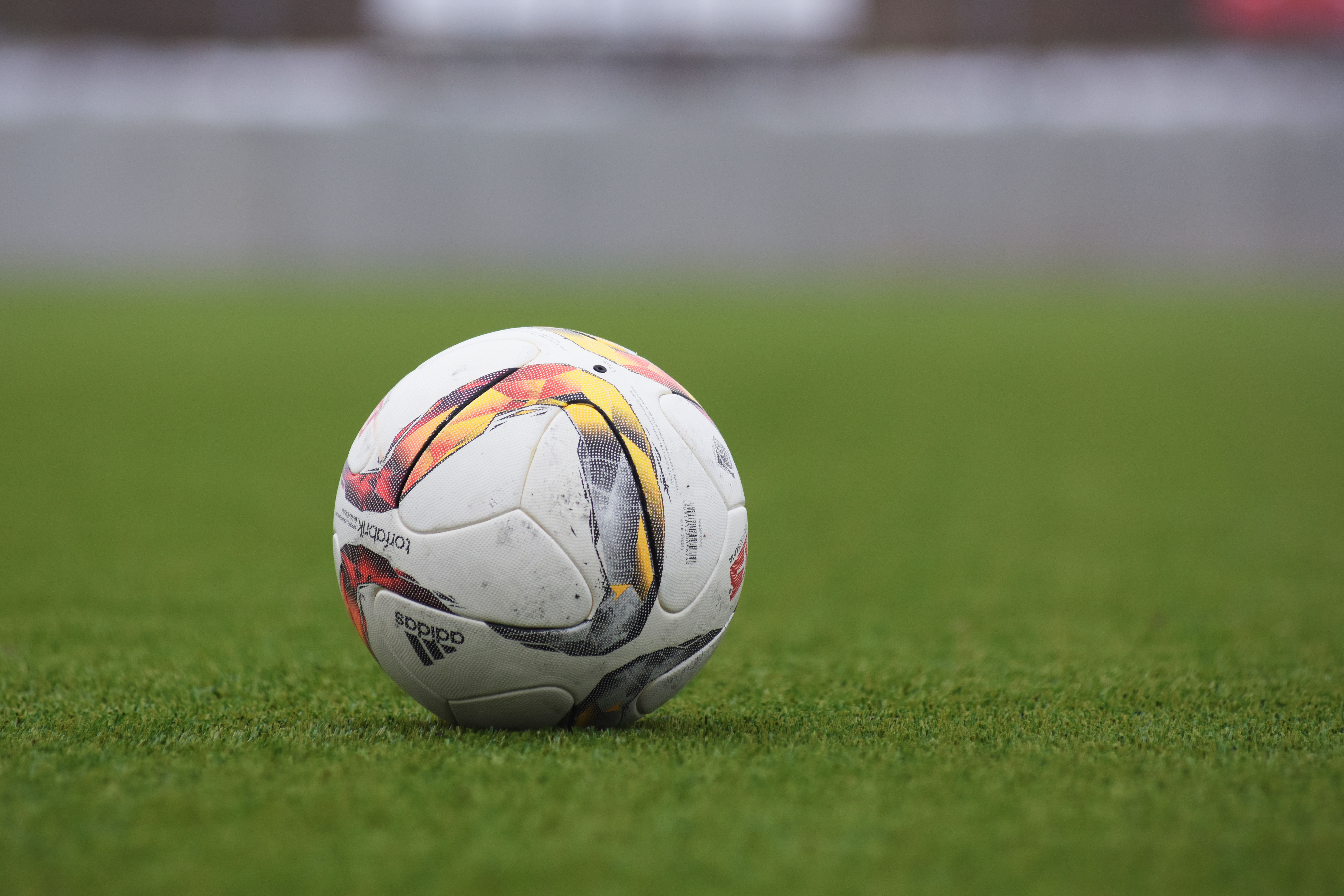 Bola Adidas sobre gramado com fundo desfocado.