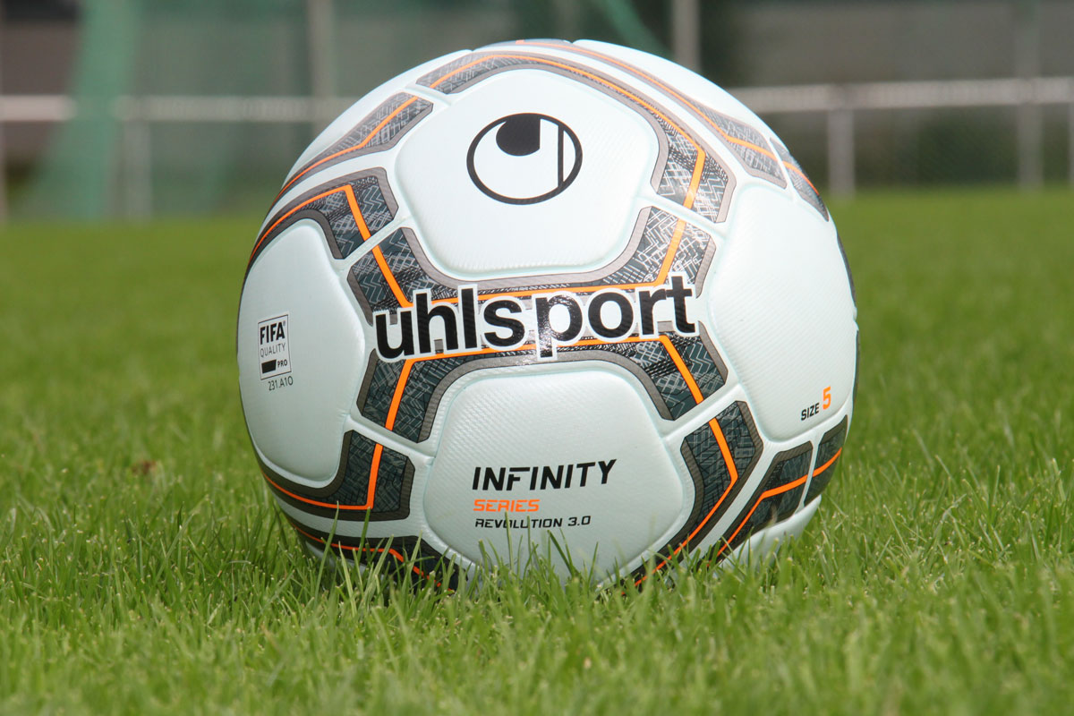 Bola Uhlsport branca e laranja sobre o gramado.