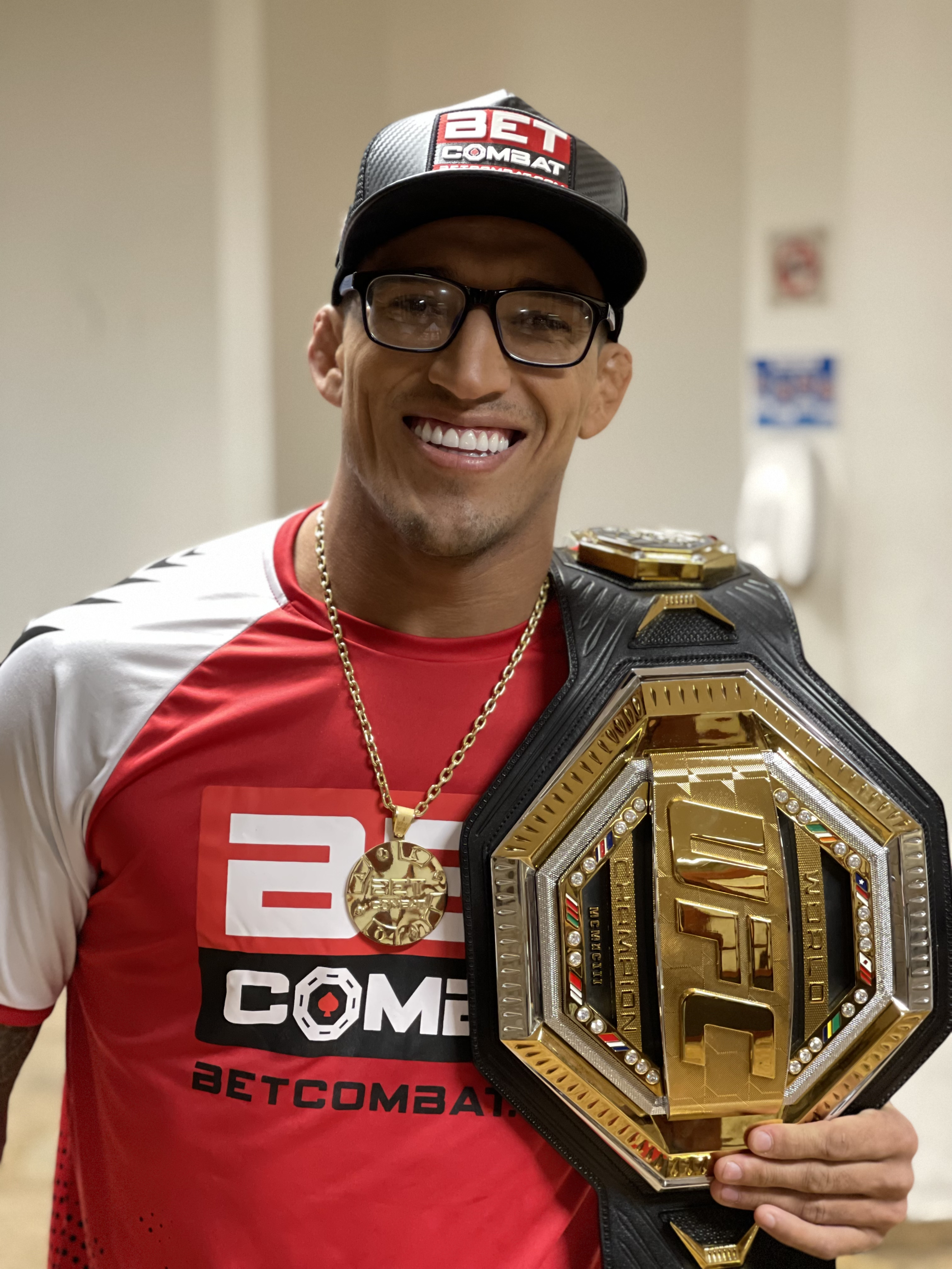 Charles Oliveira sorrindo com o cinturão do UFC sobre o ombro.