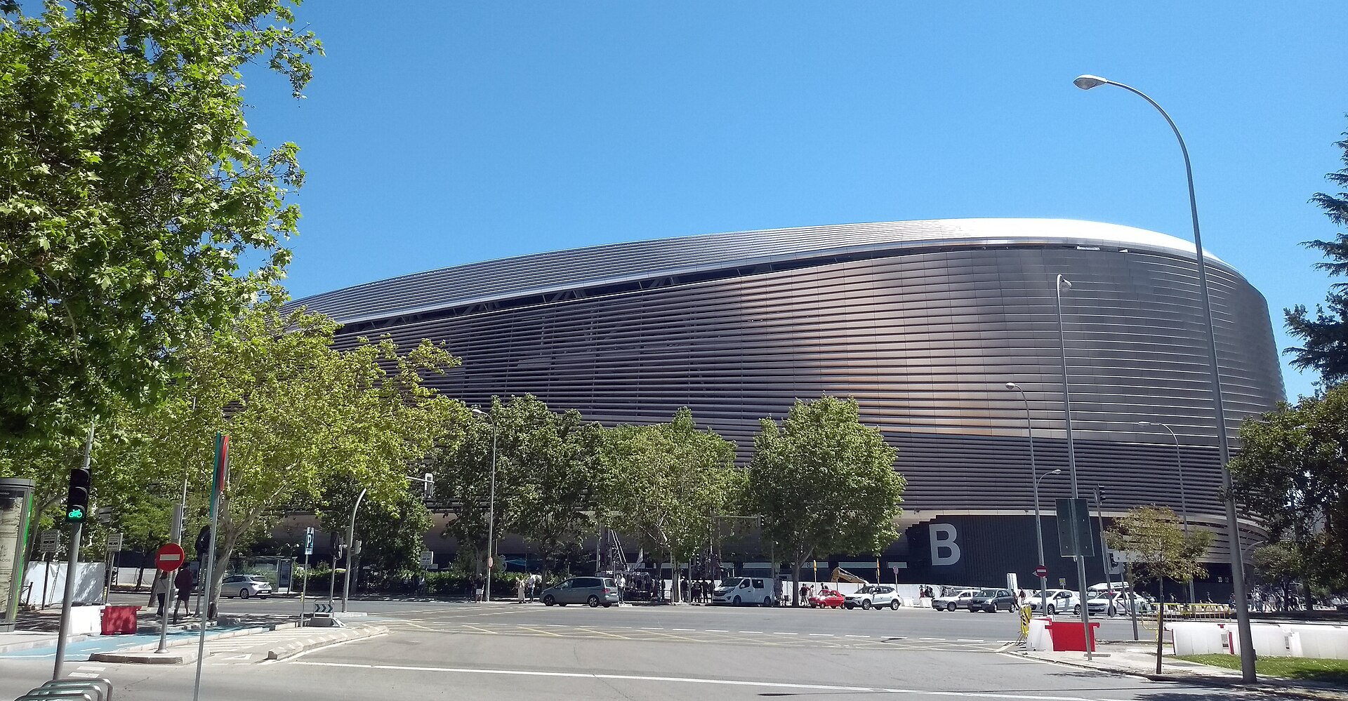 Fachada externa do Estádio Santiago Bernabéu com árvores e avenida em primeiro plano.