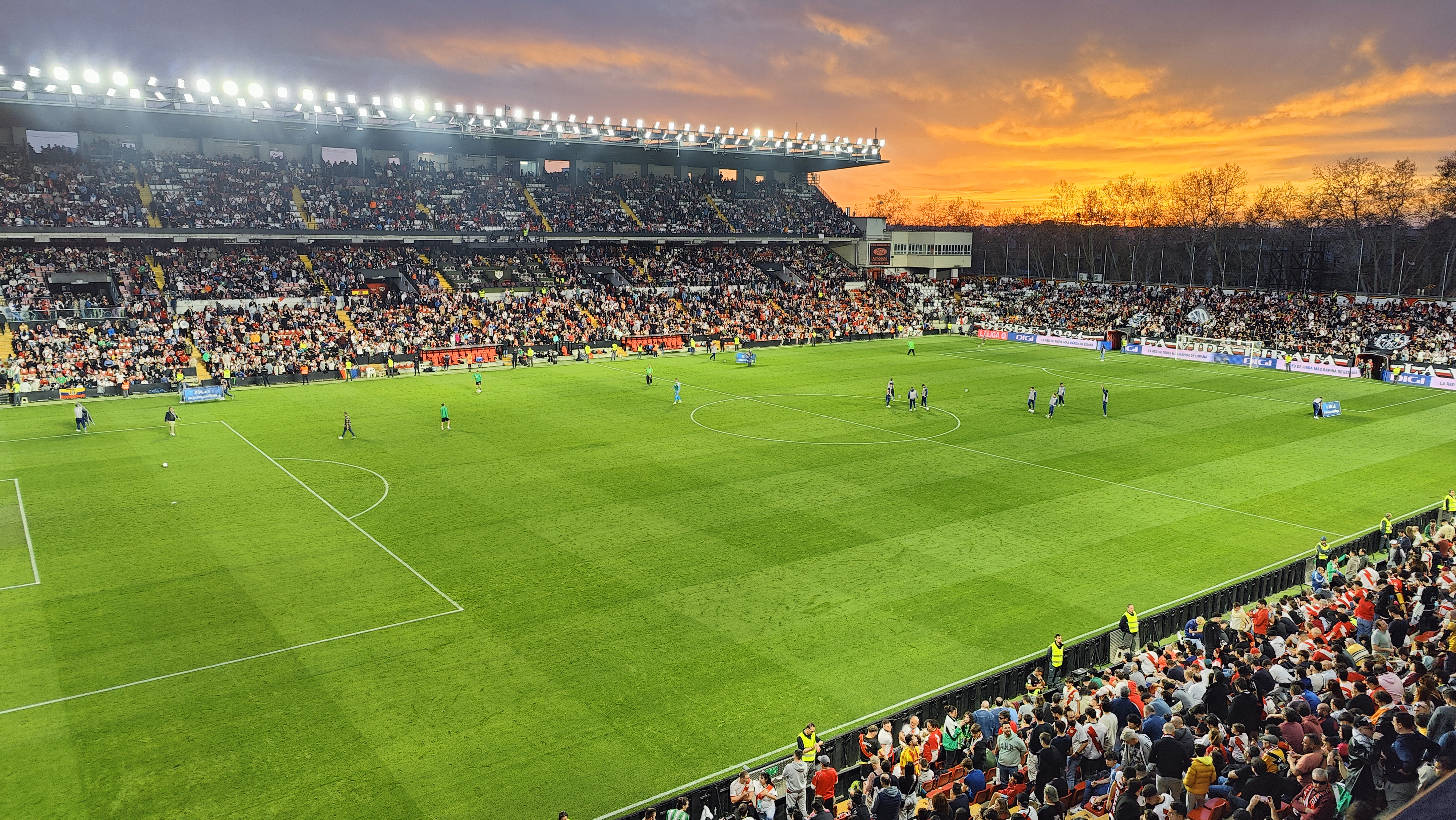 Gramado e arquibancadas do Estádio de Vallecas durante partida ao pôr do sol.