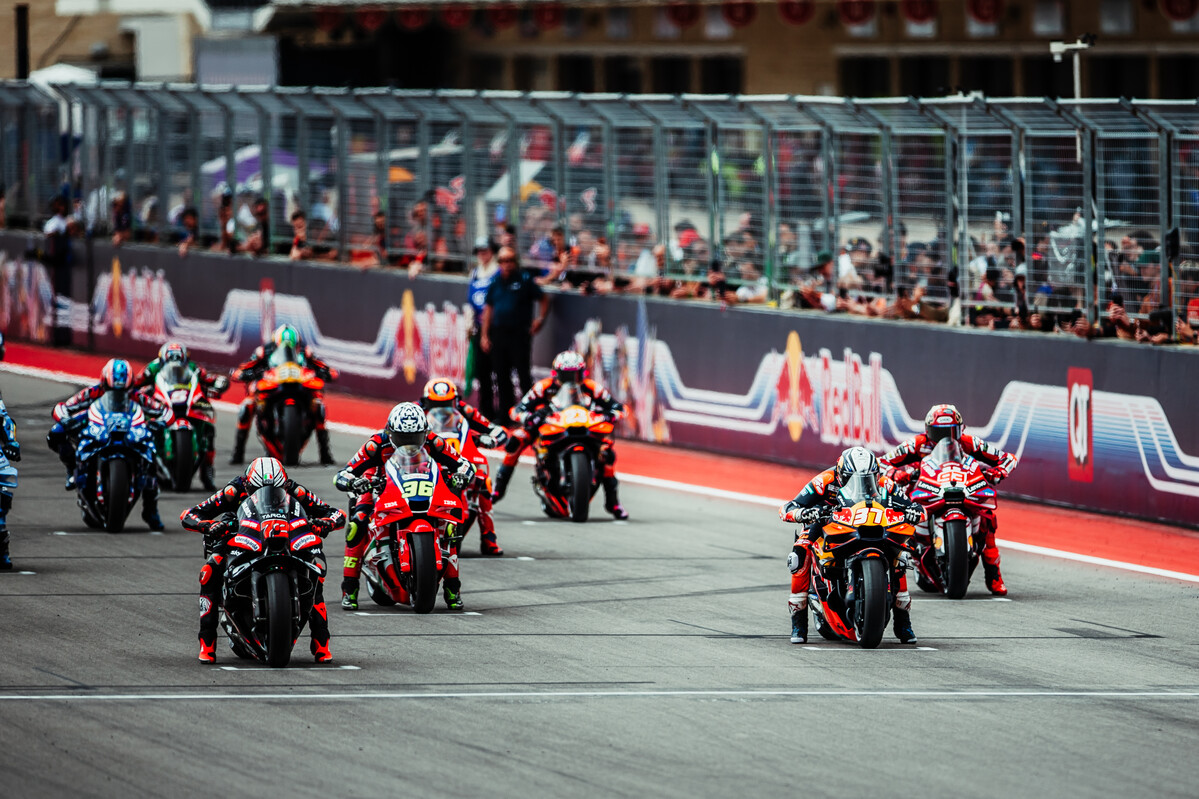 Pilotos da MotoGP aceleram juntos na reta após a largada.