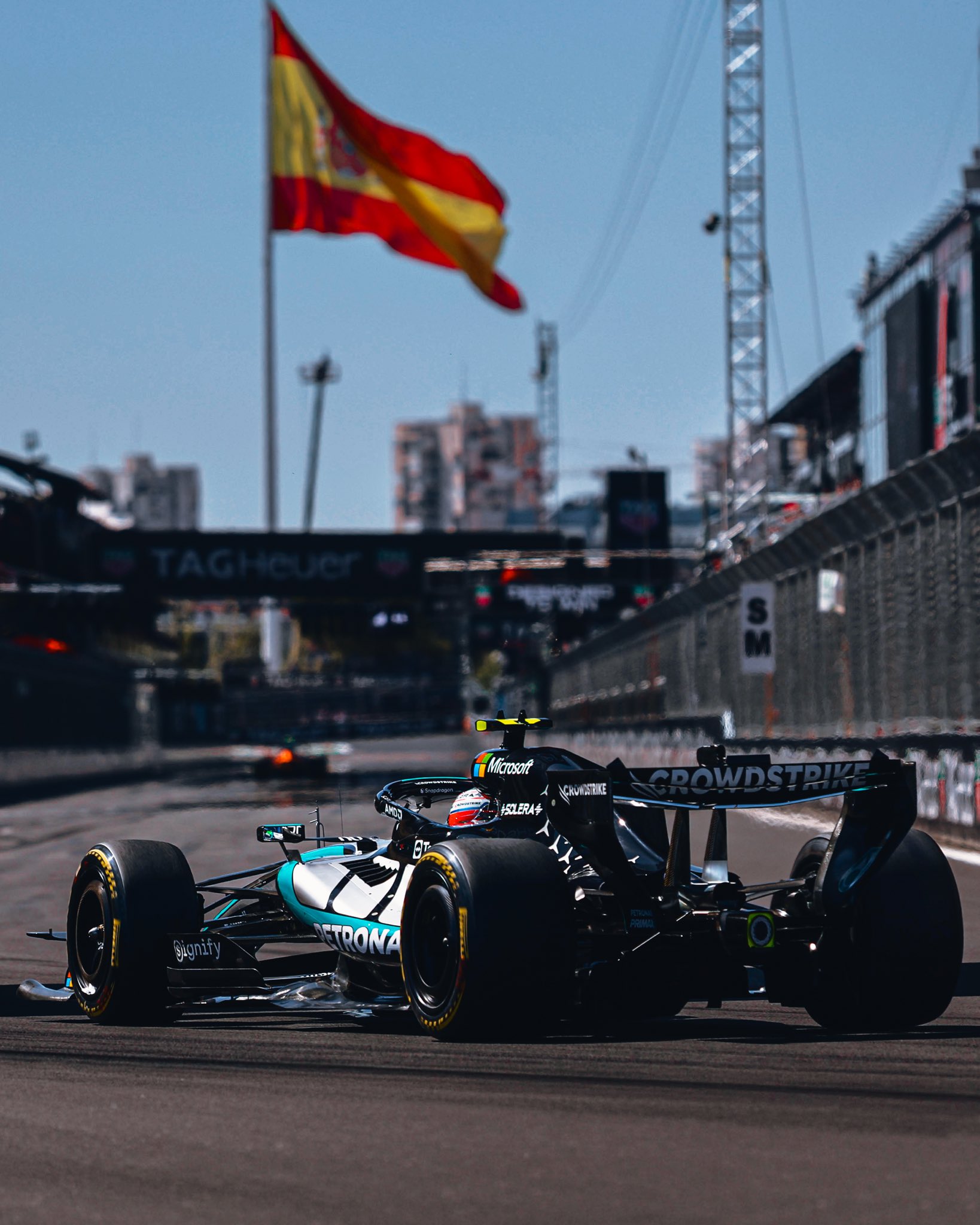 Carro da Mercedes de Fórmula 1 em pista com a bandeira da Espanha ao fundo.