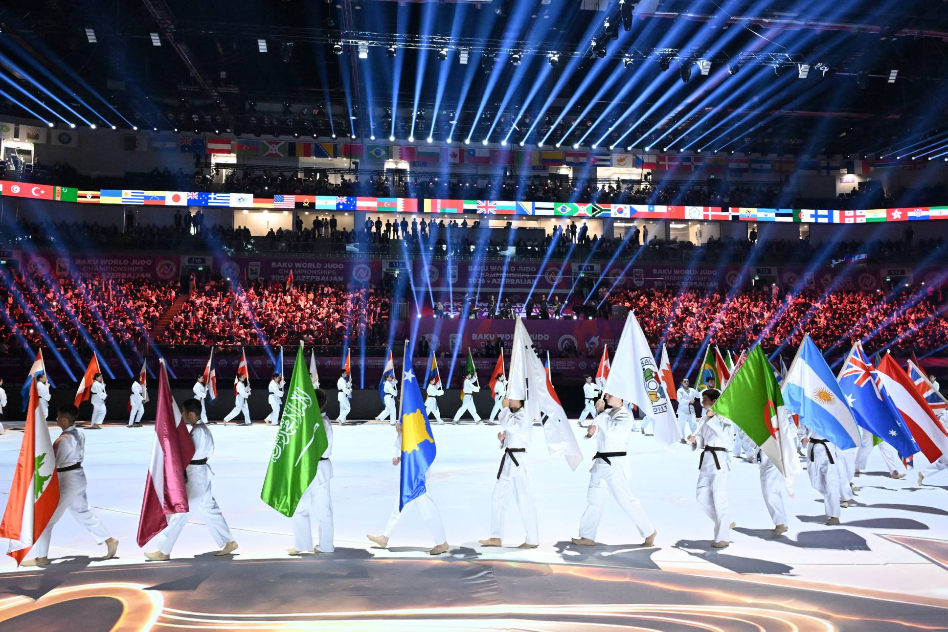Judocas carregando bandeiras de diferentes países dentro da arena.