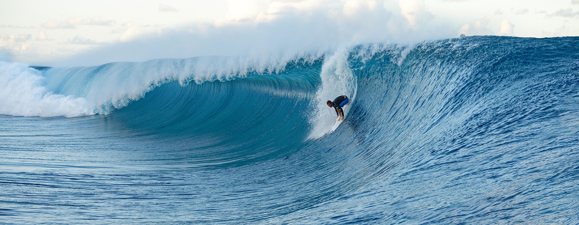 Surfista diante da extensa parede de uma grande onda em Teahupoʻo, no Taiti.