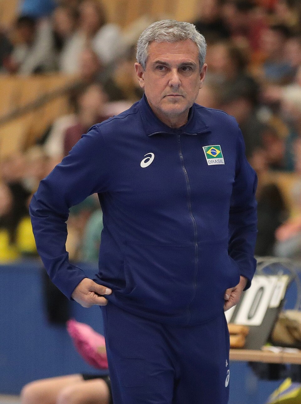 Treinador da seleção brasileira de vôlei com uniforme azul do Brasil à beira da quadra.
